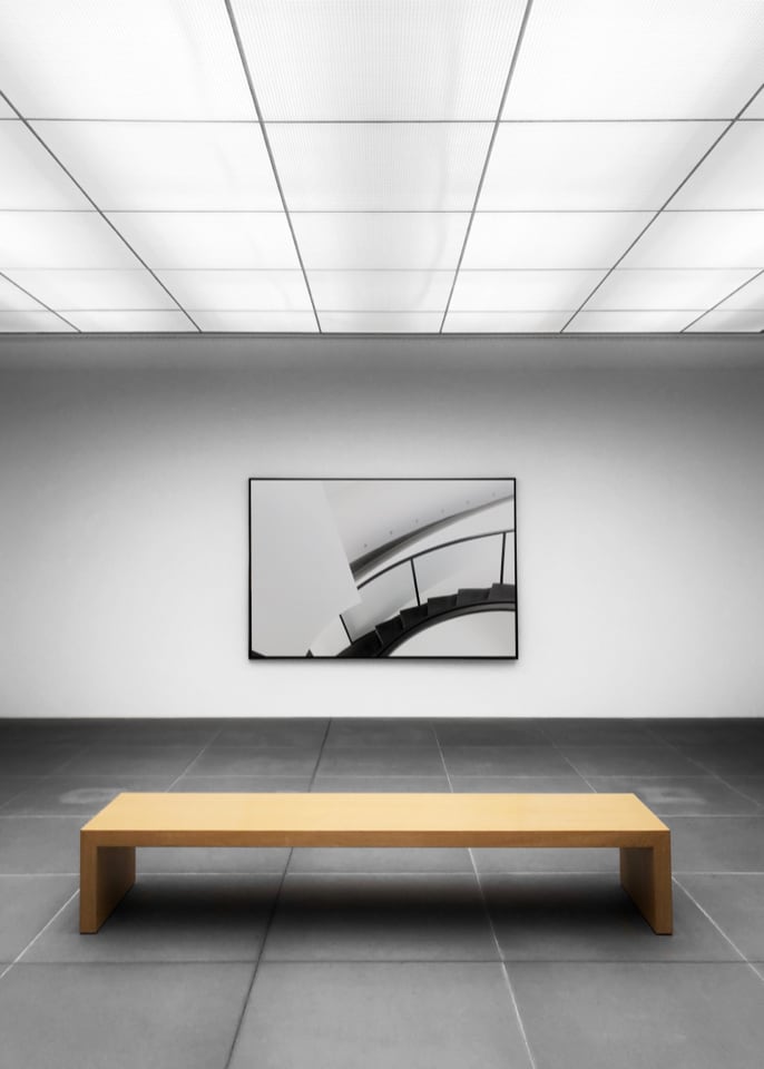 Bench in an empty gallery room with one painting on the wall.